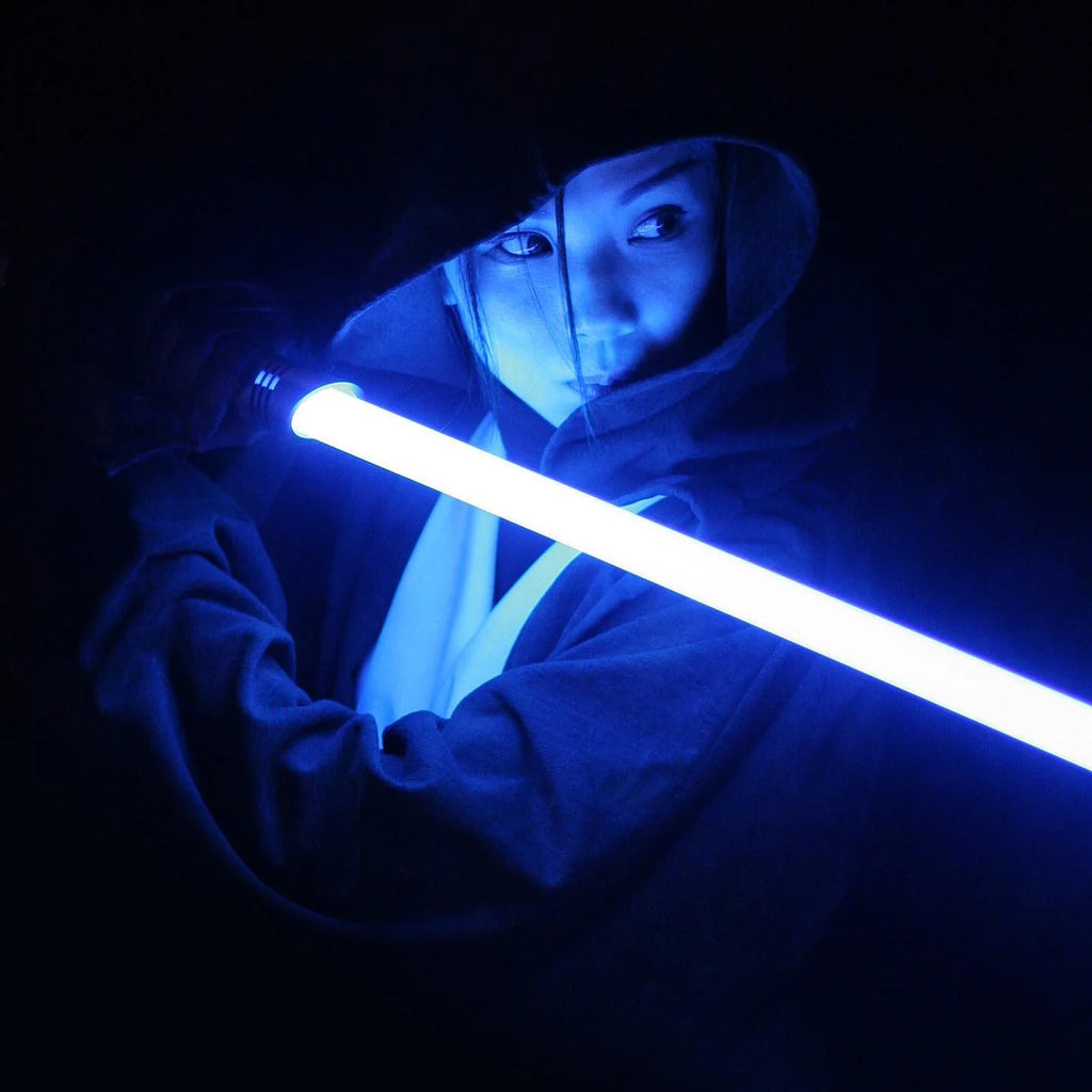 A female jedi knight illuminated by a glowing blue lightsaber.