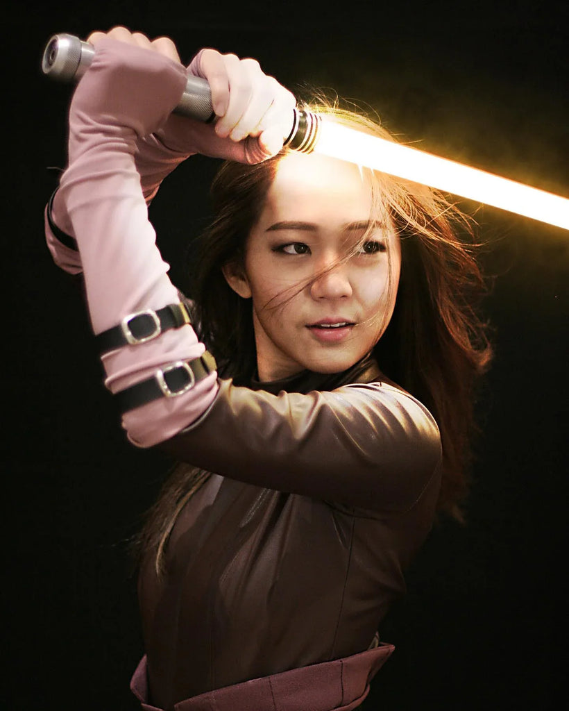 A female Jedi cosplayer with a ember lightsaber ready to strike.