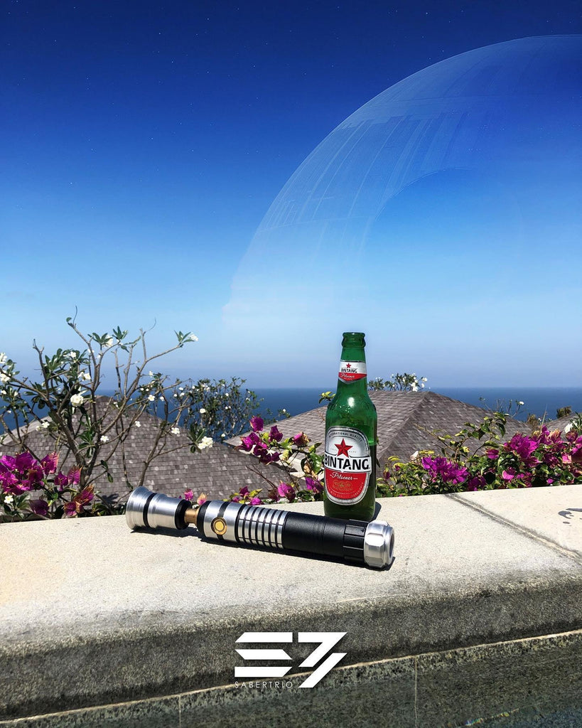 A lightsaber and beer bottle on a tropical ledge with the Death Star looming in the sky