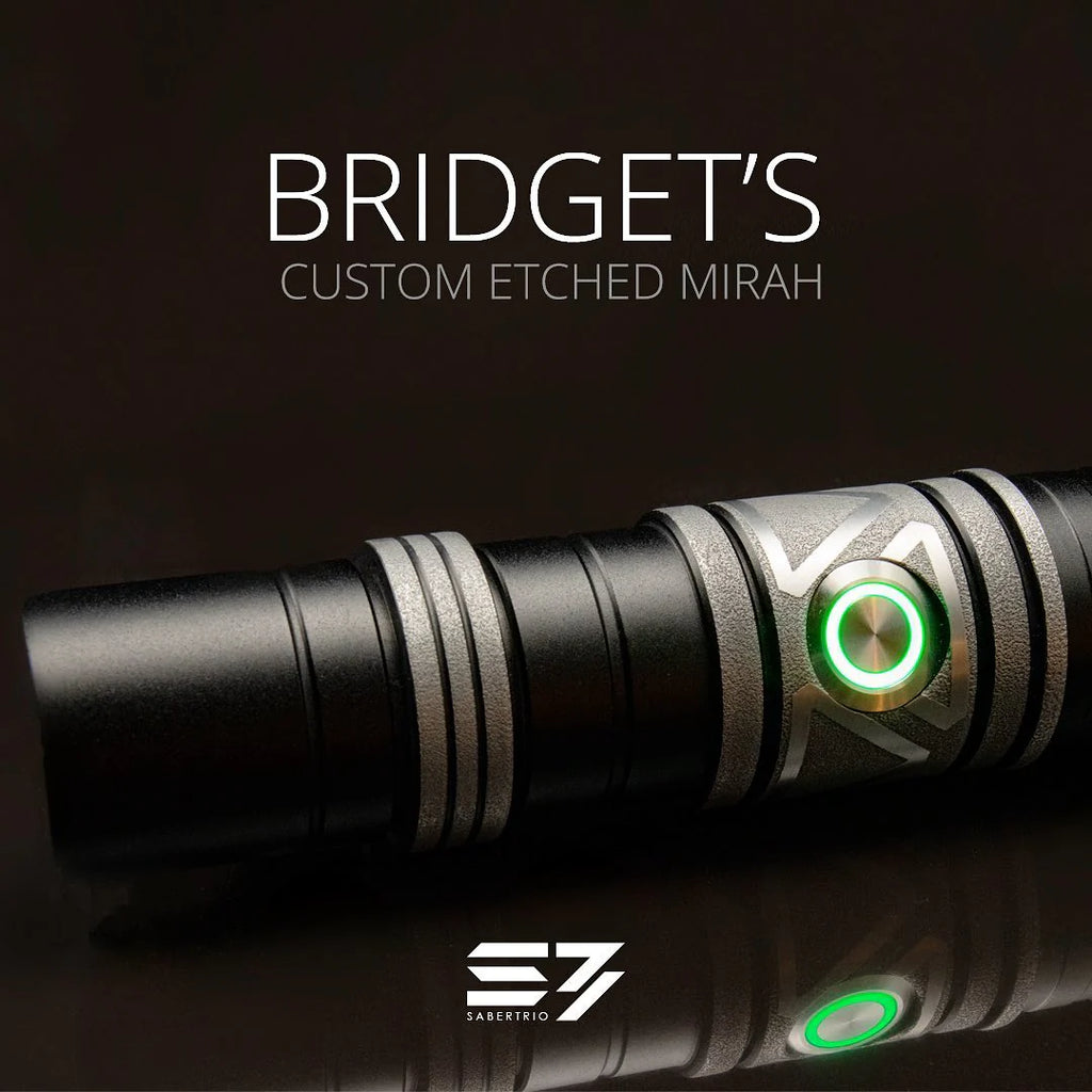 A close-up of a black and silver lightsaber hilt featuring green activation switch