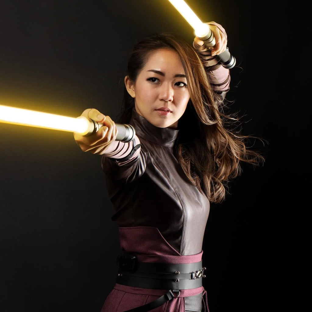 A female Jedi cosplayer wielding dual amber blades in a combat stance