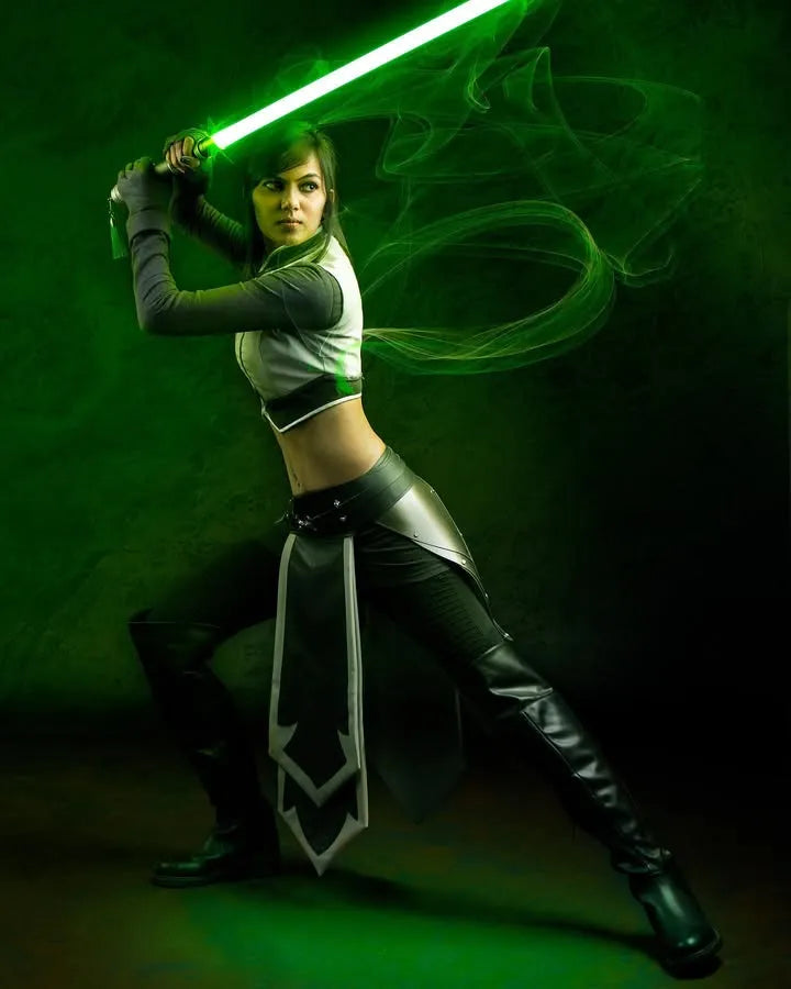 A female Jedi cosplayer looking intensely over shoulder while holding a glowing green lightsaber vertically