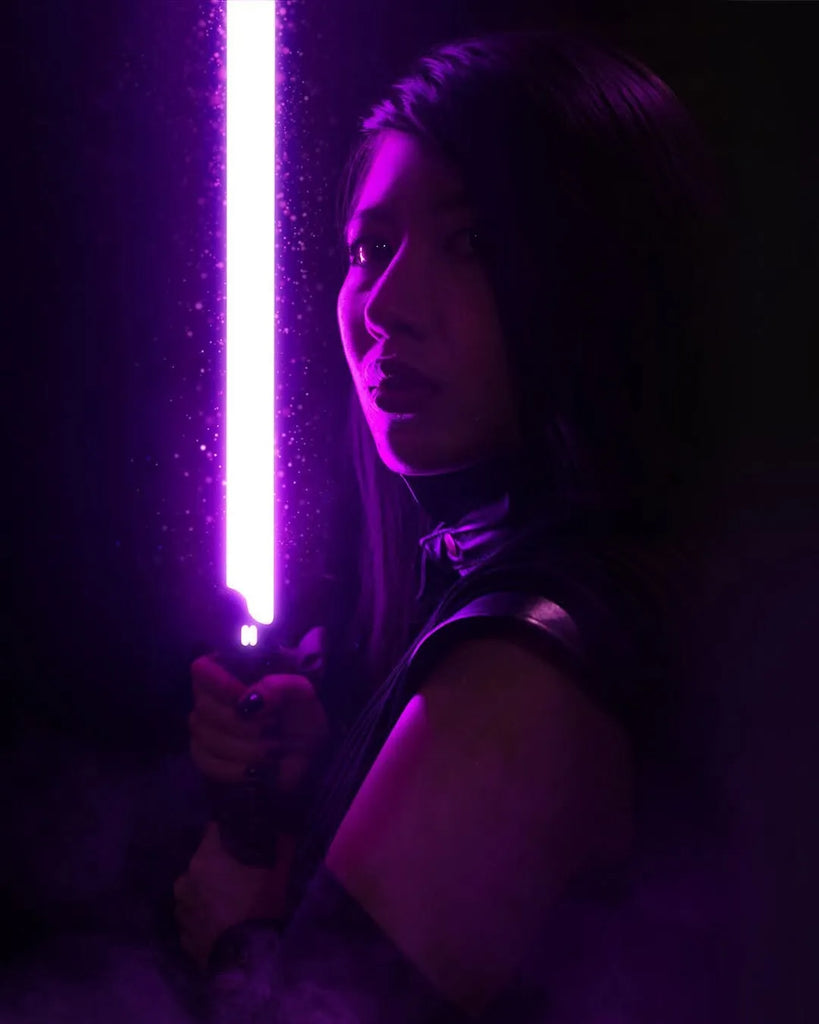 Female Mara Jade-inspired cosplayer holding a Senza, a black Rahm Kota-inspired custom neopixel lightsaber with purple blade