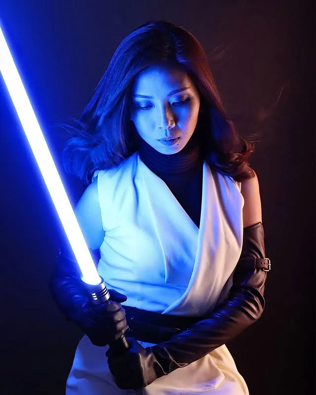 Female Jedi-inspired cosplayer holding a Darth Vader-inspired custom neopixel lightsaber with a blue blade with a contemplative expression