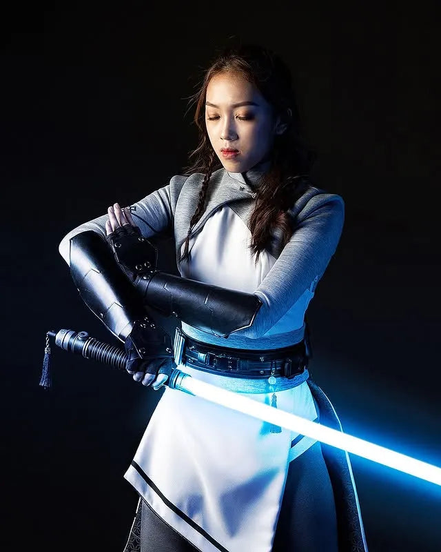 Female Jedi-inspired cosplayer holding a Rahm Kota-inspired custom neopixel lightsaber with a blue blade looking intense and focused