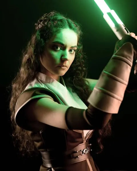 Female Jedi-inspired cosplayer holding a Cal Kestis-inspired custom neopixel lightsaber with a green blade in a defensive guard stance