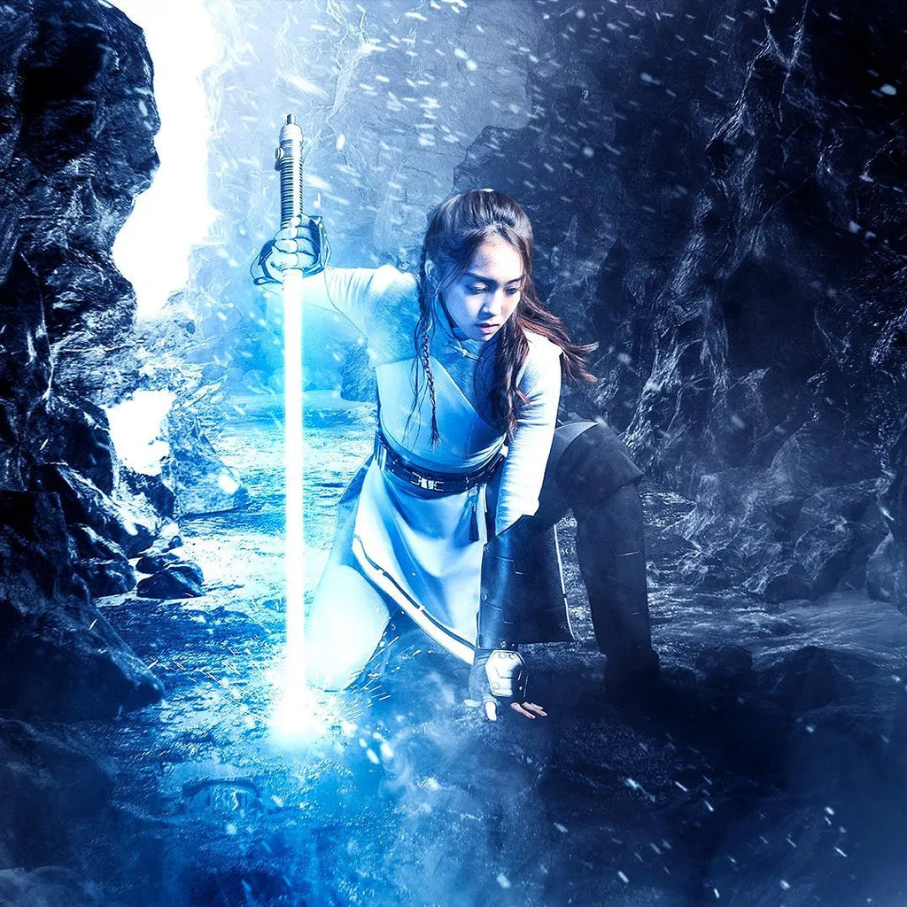 Female Jedi cosplayer kneeling in frozen environment, thrusting her Rahm Kota-inspired custom neopixel lightsaber with bright blue blade on the ground