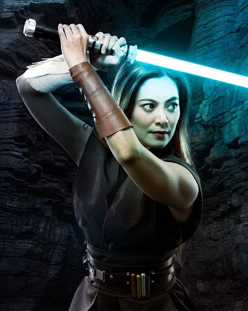 Female Jedi-inspired cosplayer in a defensive stance holding a Darth Vader-inspired custom neopixel lightsaber with bright cyan blade