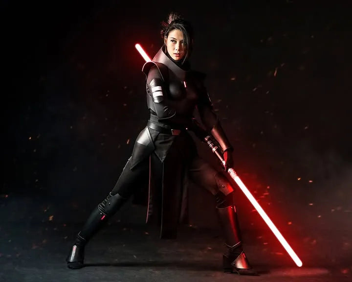 Sith Inquisitor-inspired cosplayer in black armor standing in combat stance. She holds a Sith-inspired custom neopixel lightsaber with red blade