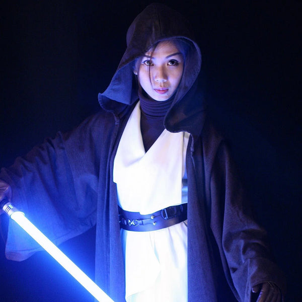 A female Jedi cosplayer wearing a dark brown hooded robe, holding an ignited blue lightsaber