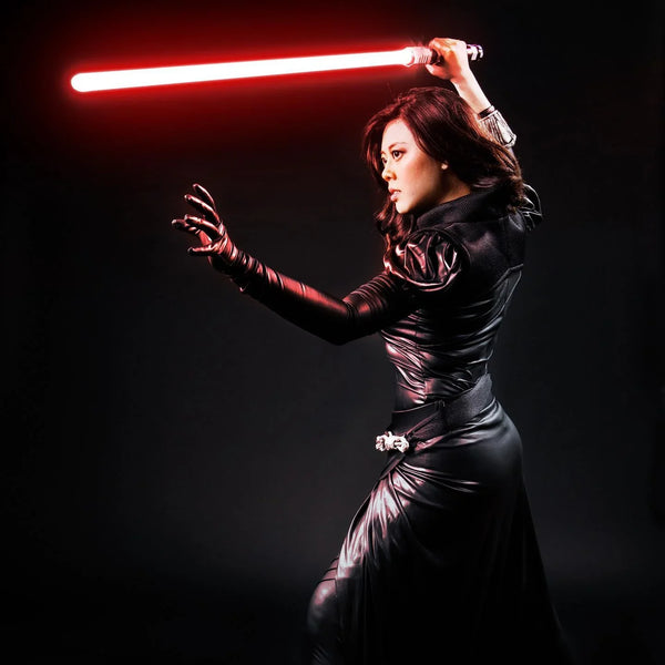 A female Sith warrior in black armor reaching out with the Force while wielding a red lightsaber